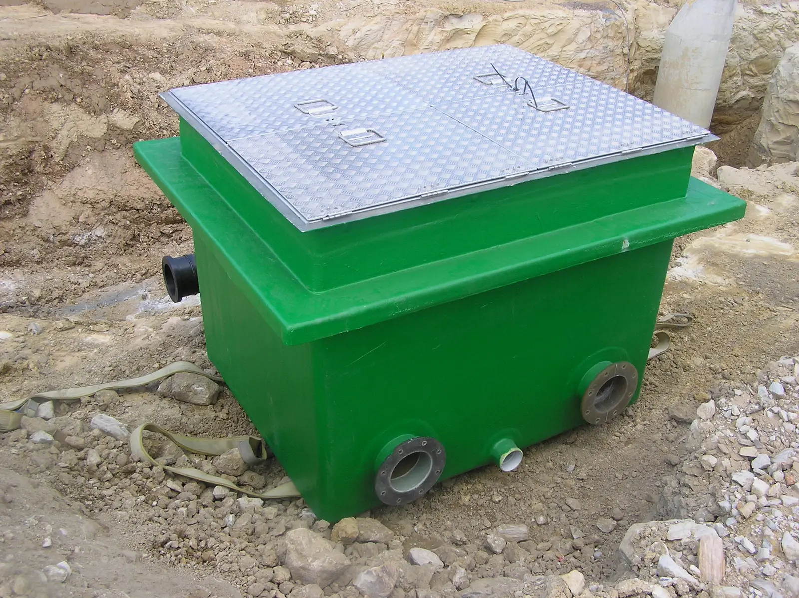 Mullaly fibreglass valve pit with aluminium checker-plate access cover and flanged pipe connections, bedded in its excavation